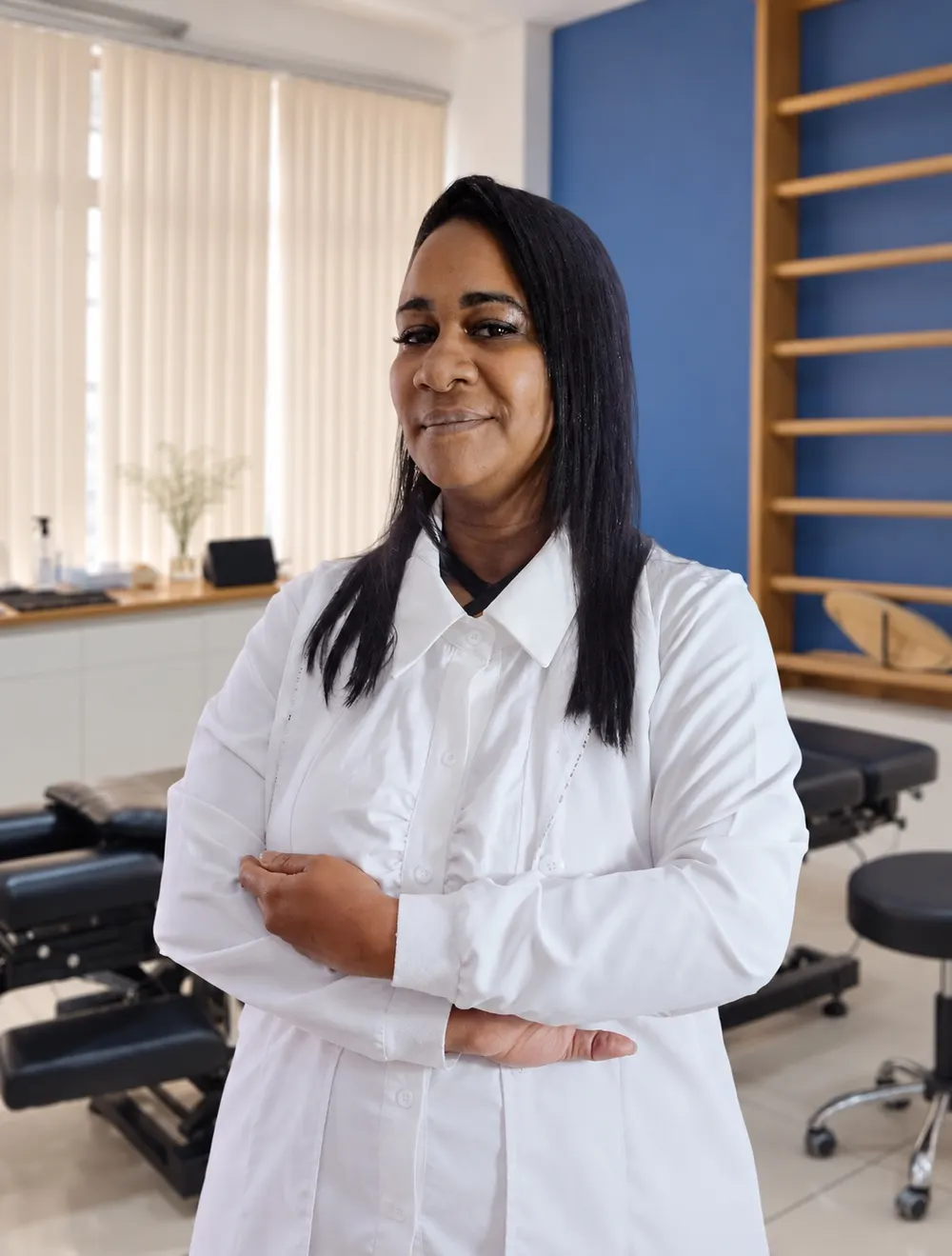 Dra. Raisa Braz no consultório, de braços cruzados e sorrindo